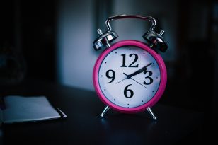 A close up photograph of a traditional pink analogue alarm clock.
