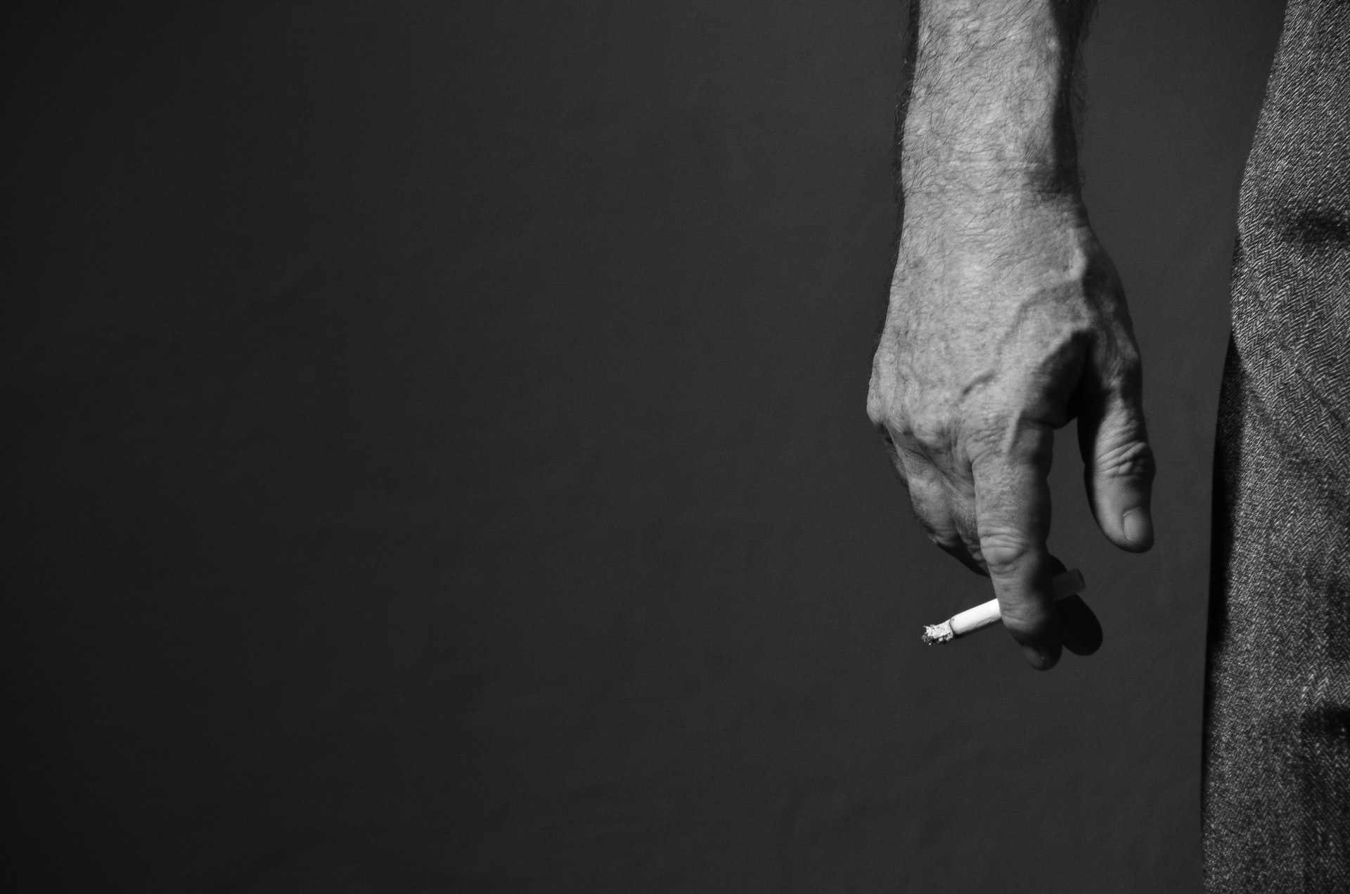 A man holding a lit cigarette by his side.