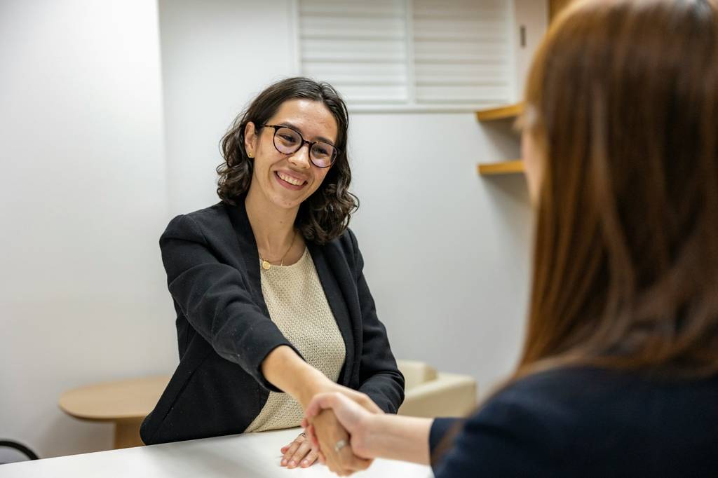 Two woman shaking hands and smiling in office